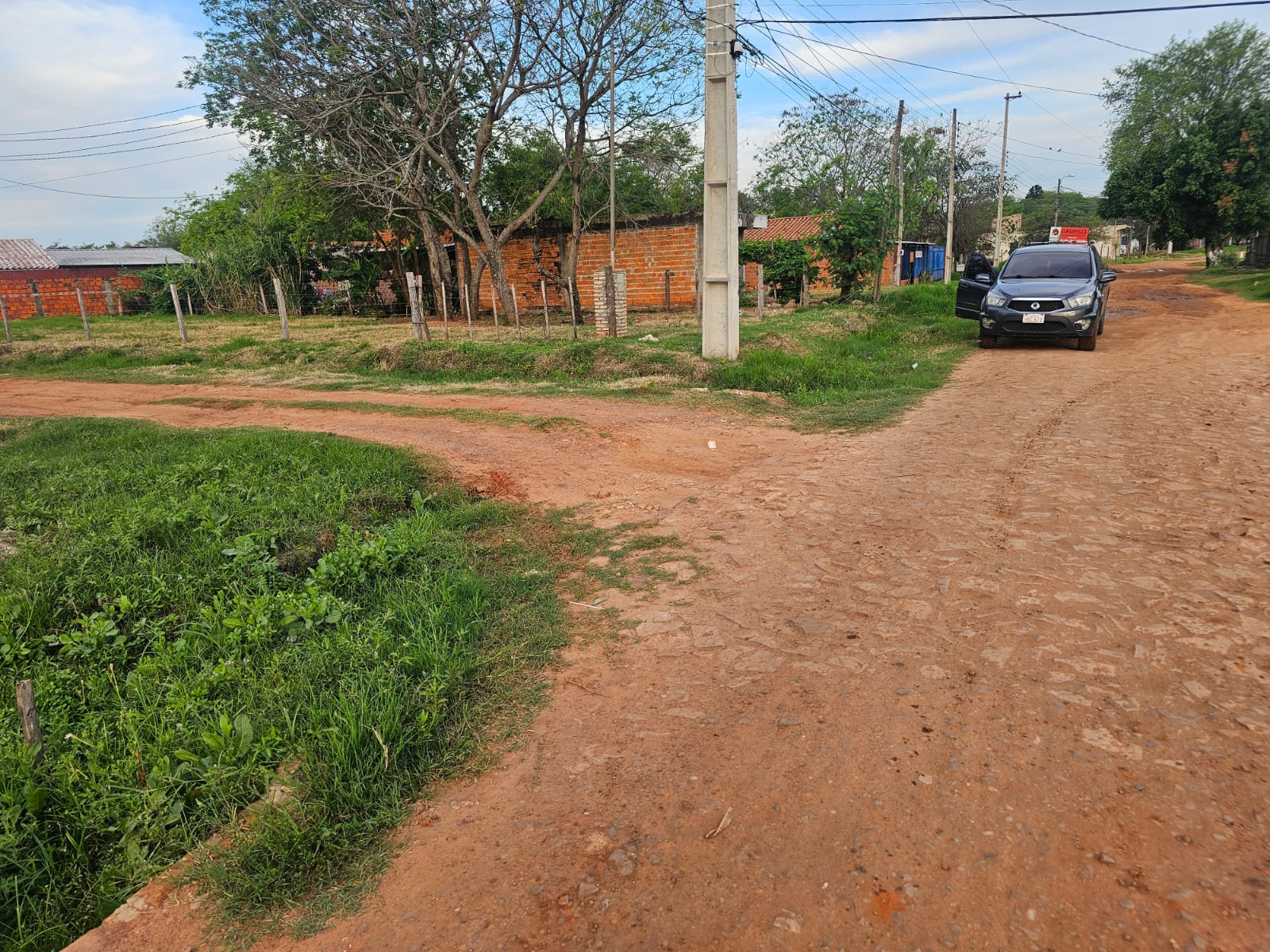 Calle de tierra de acceso con viviendas y árboles del entorno